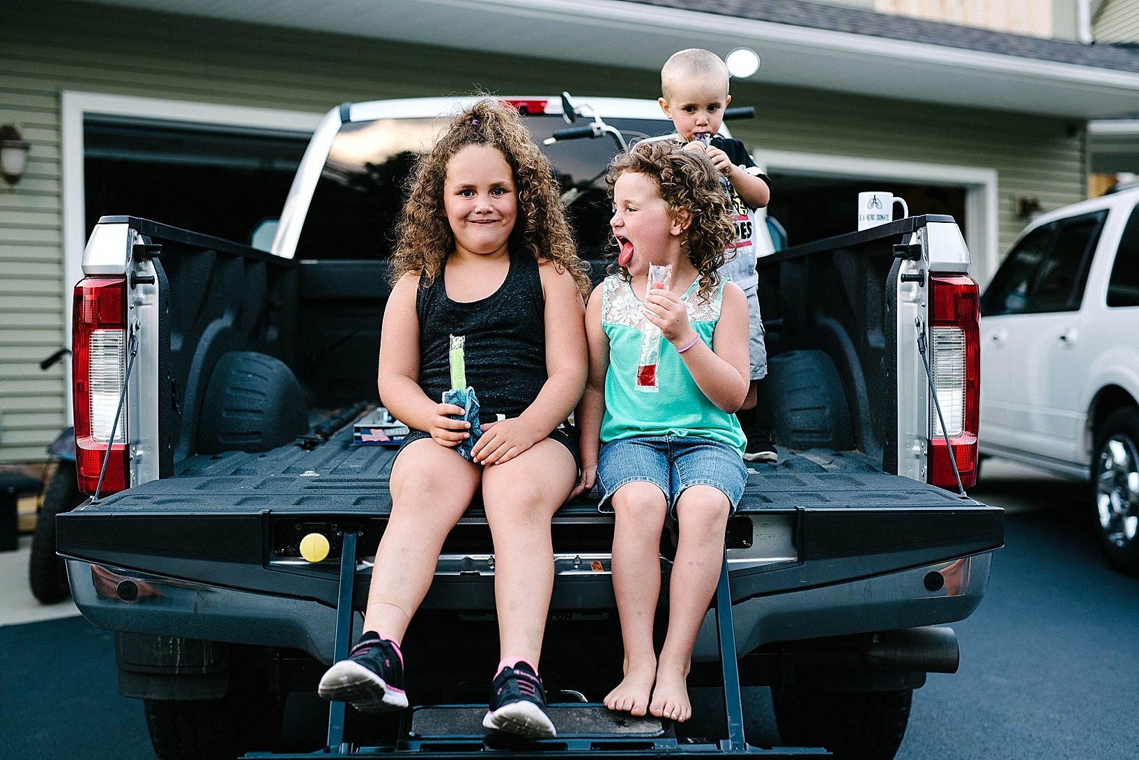 kids sitting on back of pickup truck eating popsicles
