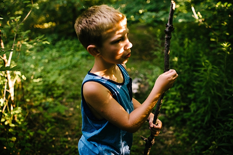 boy walking through the woods with a walking stick