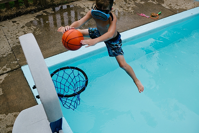 little boy slam dunking basketball in swimming pool