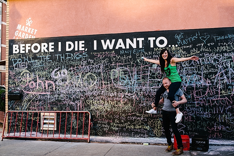 girl sitting on guy's shoulders in front of chalkboard wall