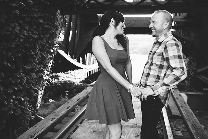 girl wearing red dress and heels with fiance in blue plaid by ivy covered bridge