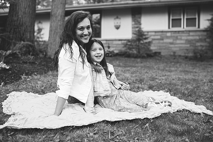 mom and daughter sitting on yellow blanket in front yard