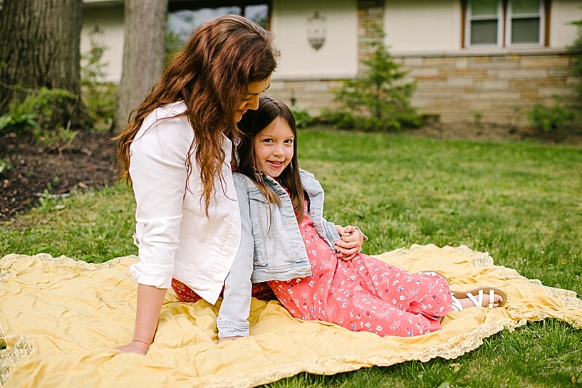 mom and daughter sitting on yellow blanket in front yard