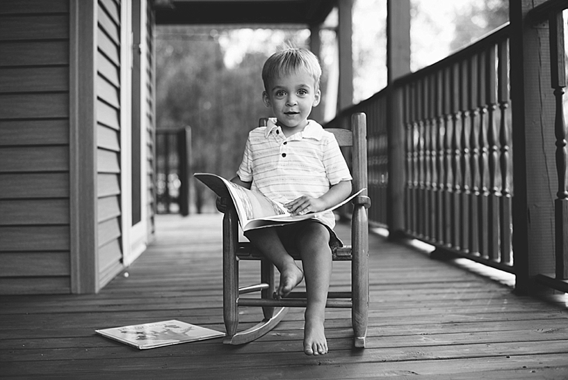 little boy sitting in rocking chair on front porch reading book