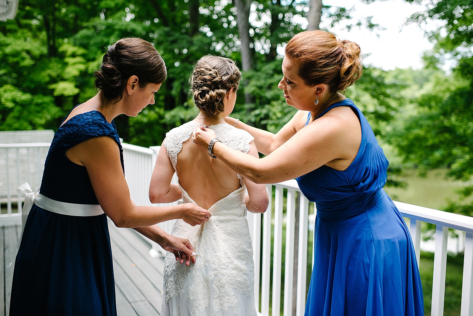 bridesmaids in blue dresses helping bride into her dress