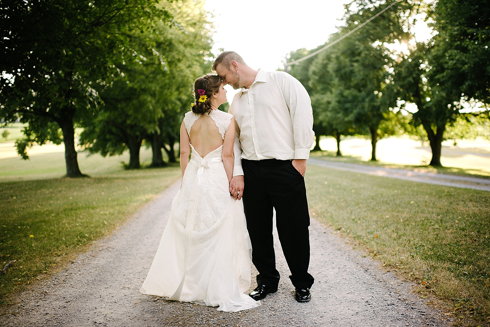 bride and groom standing on dirt country road at sunset