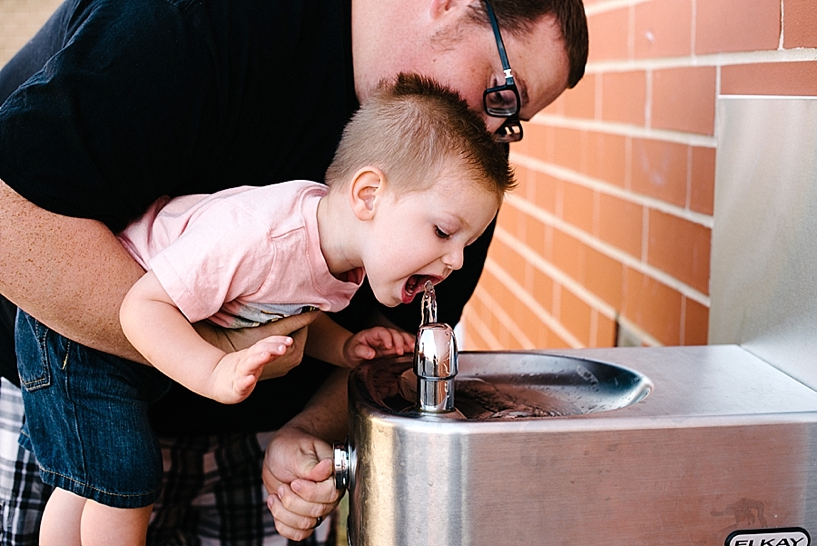 dad helping son drink from water fountain