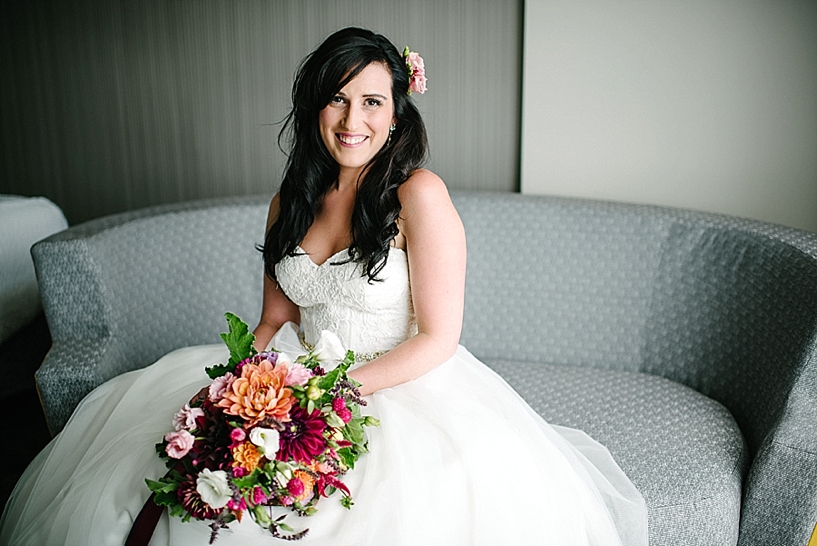 bride sitting in hotel room holding her bouquet and smiling