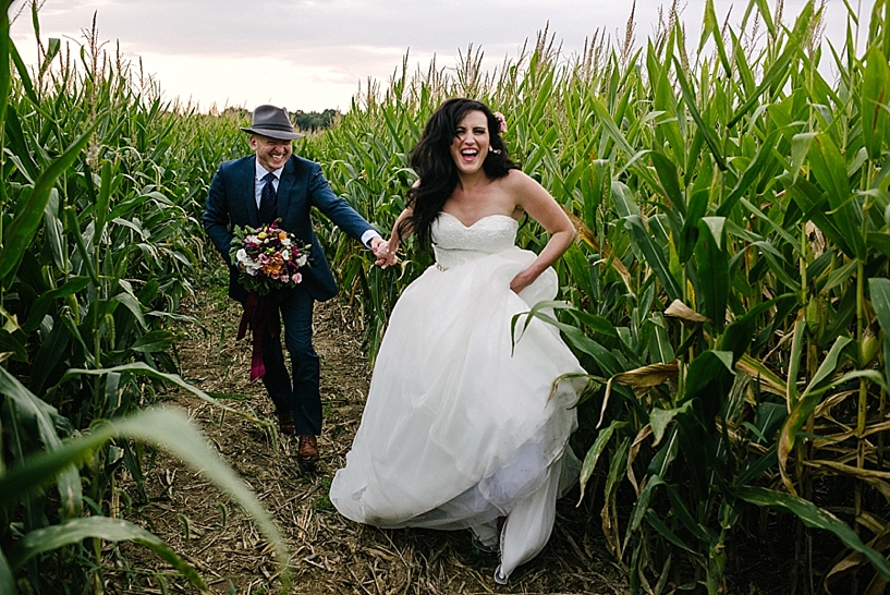 bride and groom running through corn maze laughing