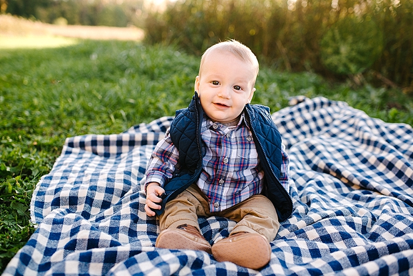6 month old little boy in plaid shirt and navy vest sitting on blue and white checked blanket