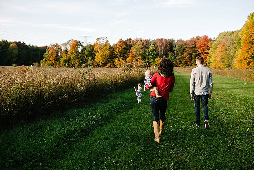 family of four walking through field with fall trees in the background