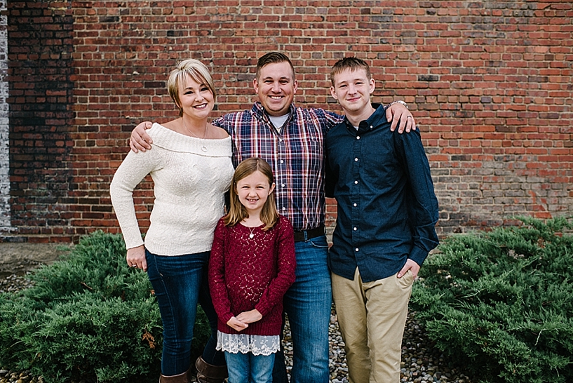 family in maroon, navy, and cream standing in front of brick wall