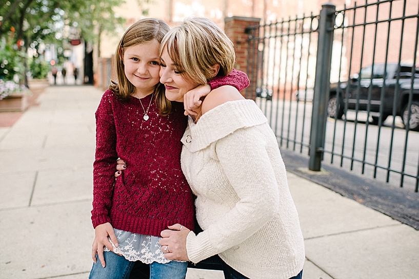girl in maroon sweater hugging mom on city sidewalk