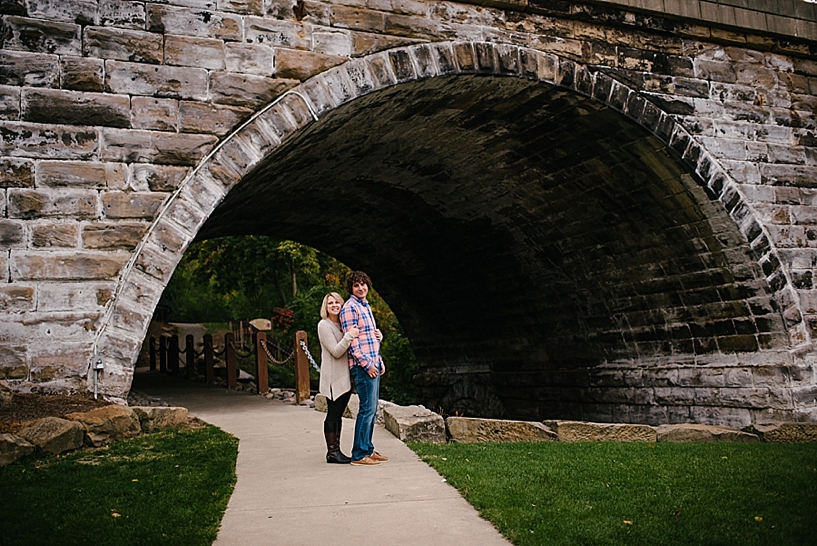 girl in oversized sweater and guy in pink and blue plaid shirt standing underneath stone tunnel