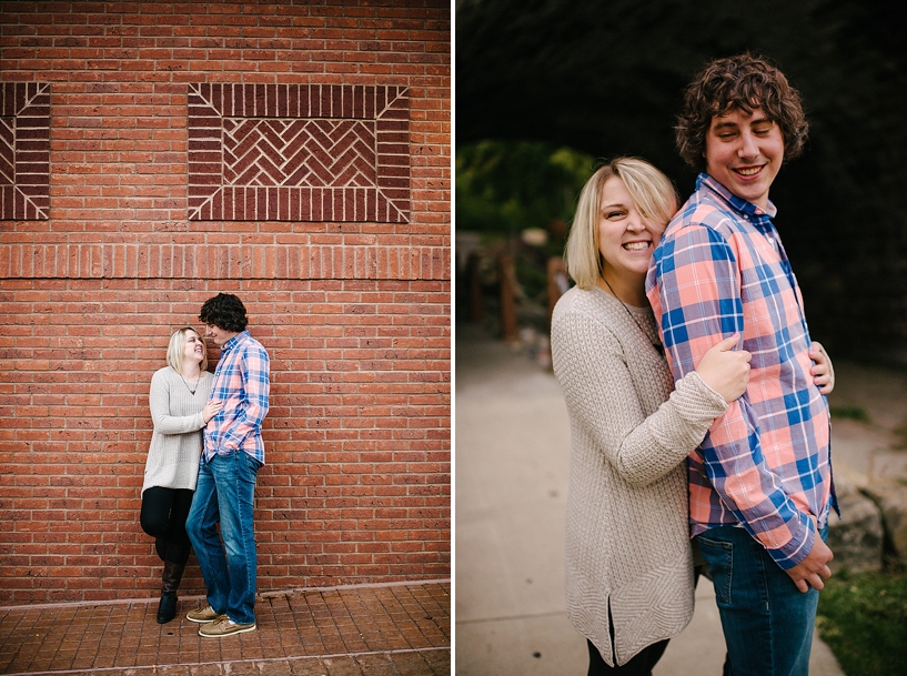 girl in oversized sweater and guy in pink and blue plaid shirt leaning against brick wall