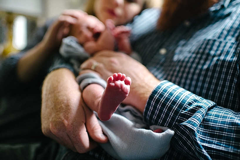 newborn in father's arms with foot sticking up in the air