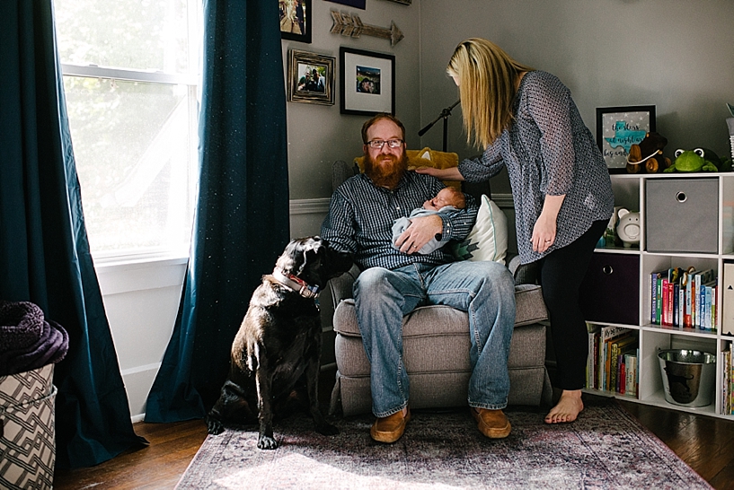 dad sitting in rocker in nursery holding baby with dog sitting nearby