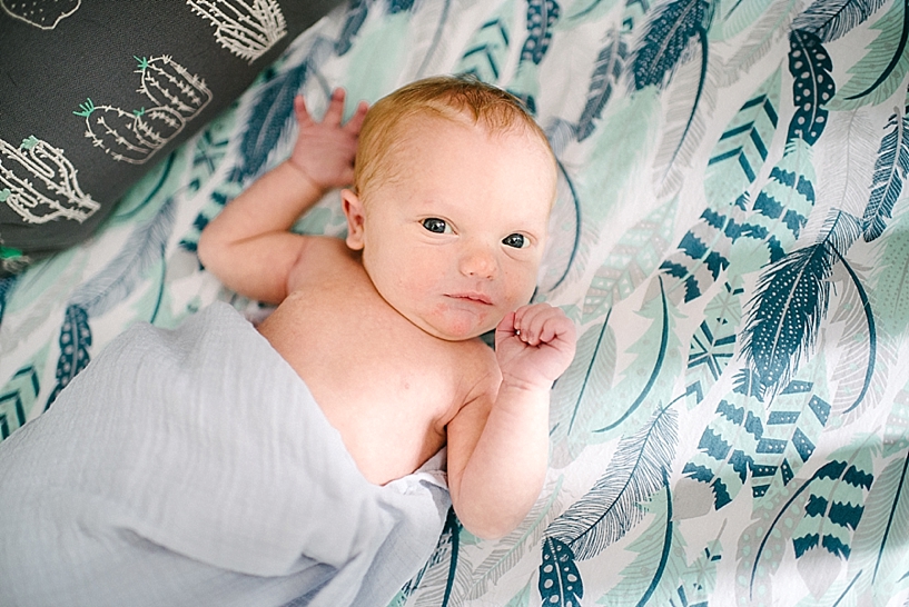 newborn baby in crib with aqua feather sheets and eyes wide open