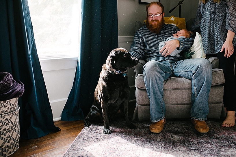 dad sitting in rocker holding baby with dog nearby