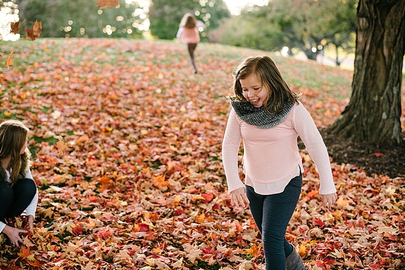 girl in pink shirt and grey scarf running through the leaves