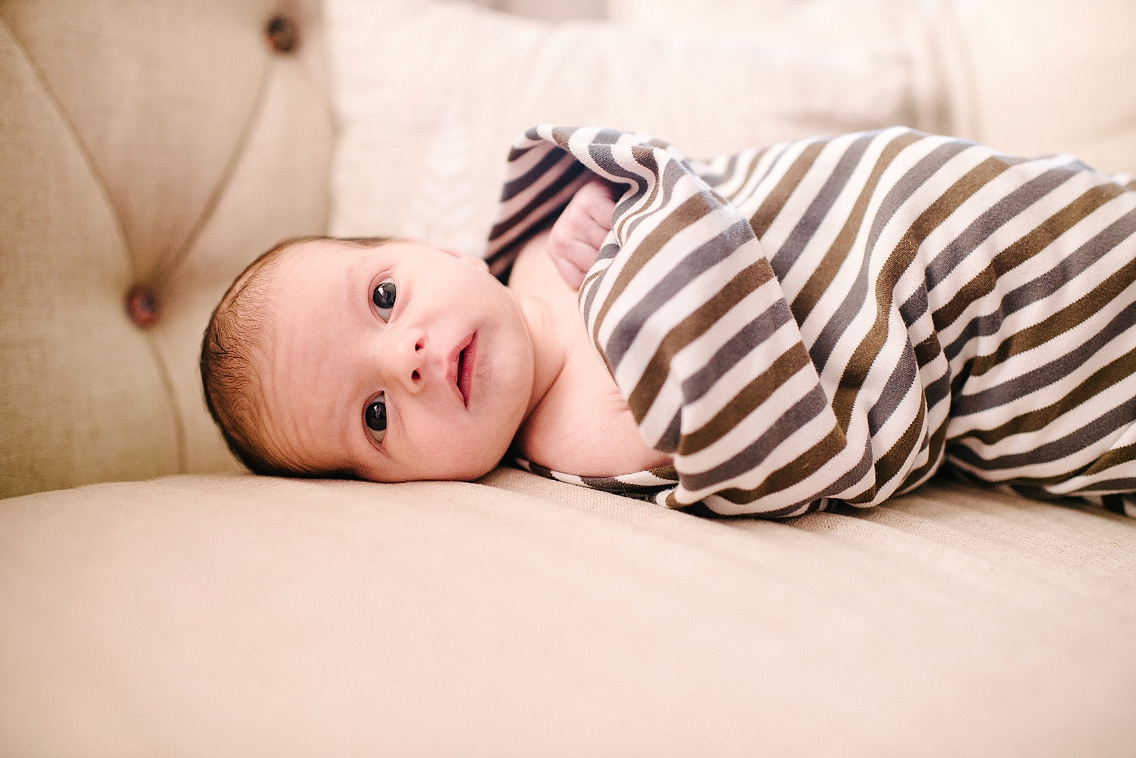 newborn baby boy wrapped in brown striped blanket laying on couch with eyes wide open