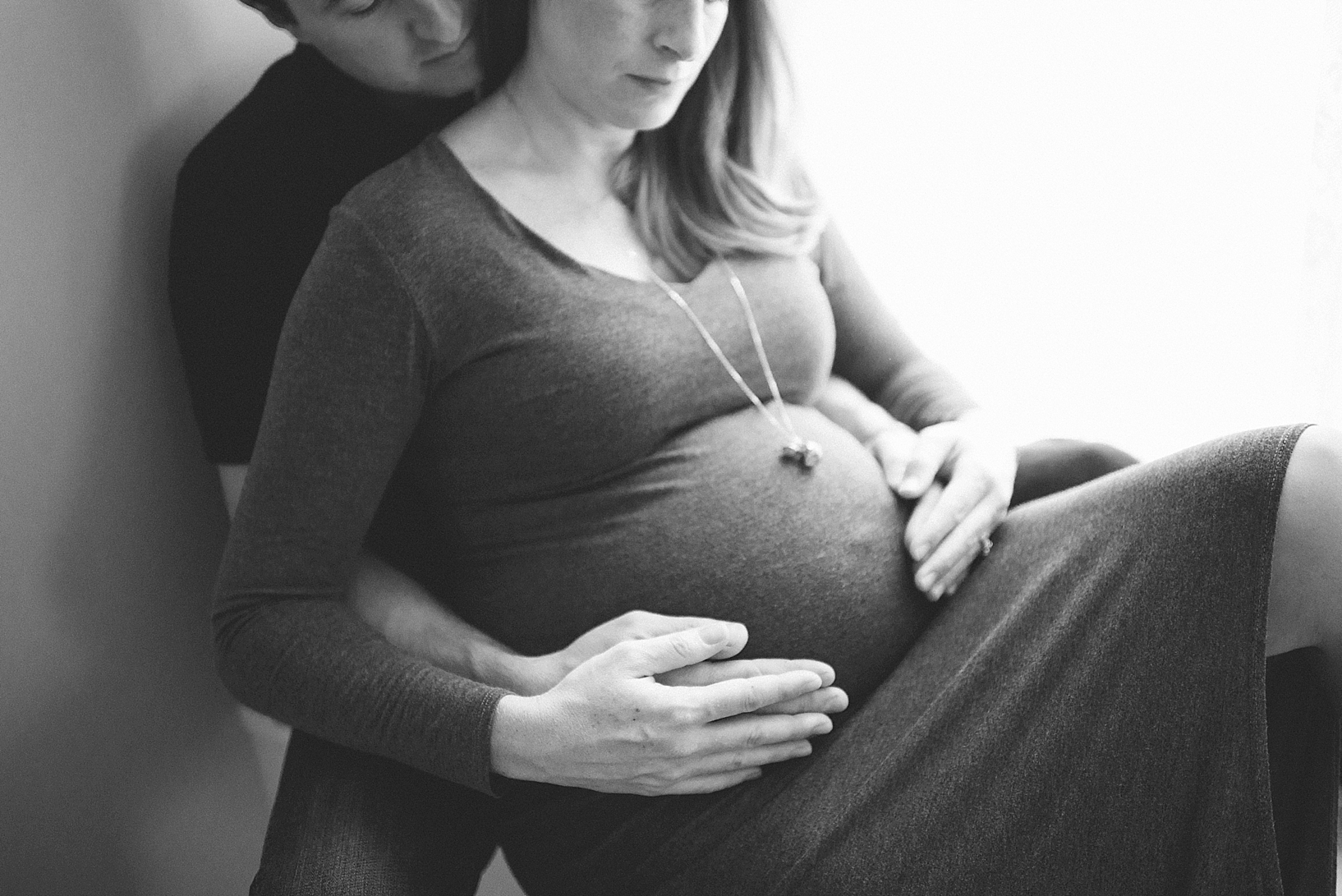 expectant mother in long grey dress with husband's arms wrapped around belly