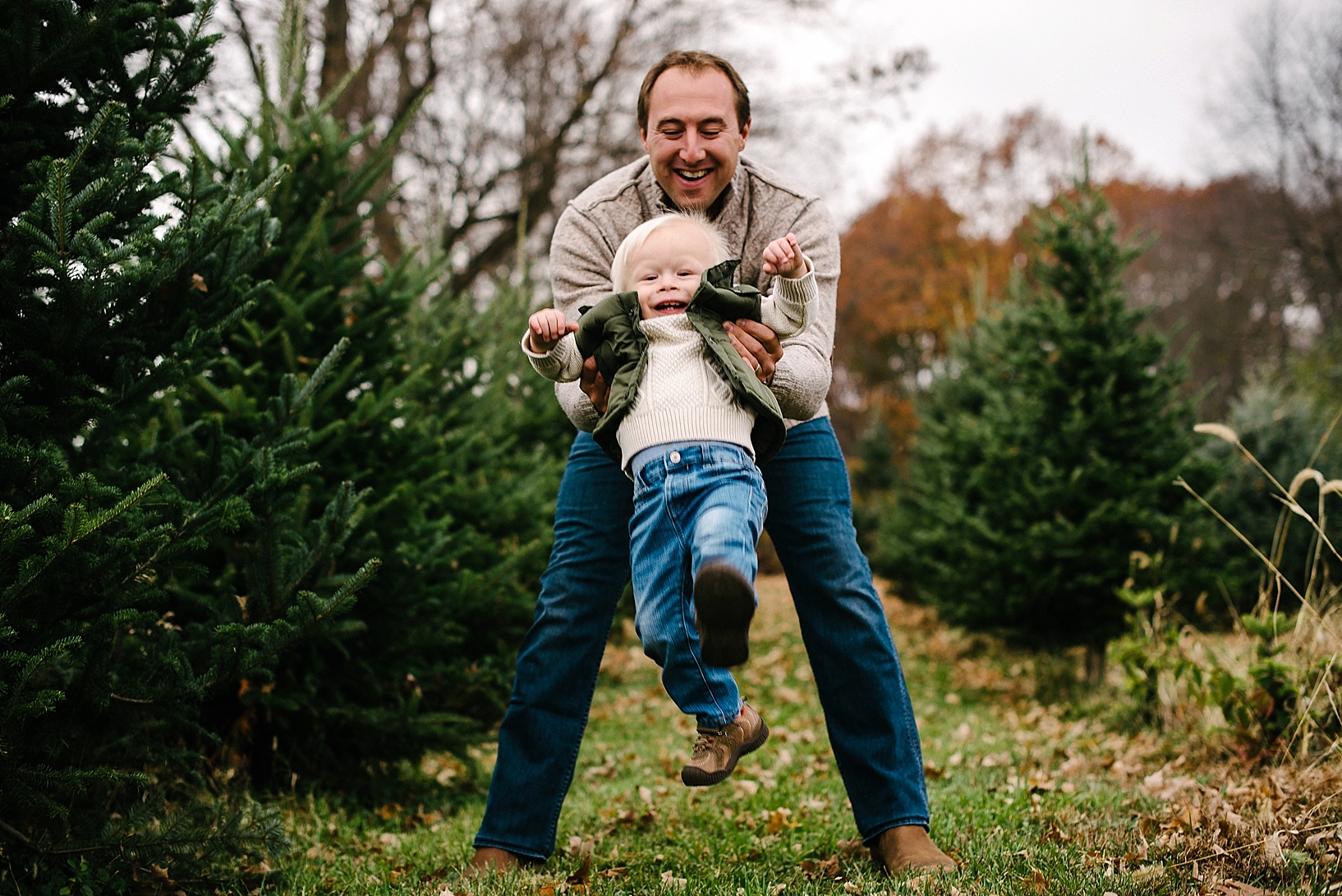 father swinging toddler son in the air among pine trees
