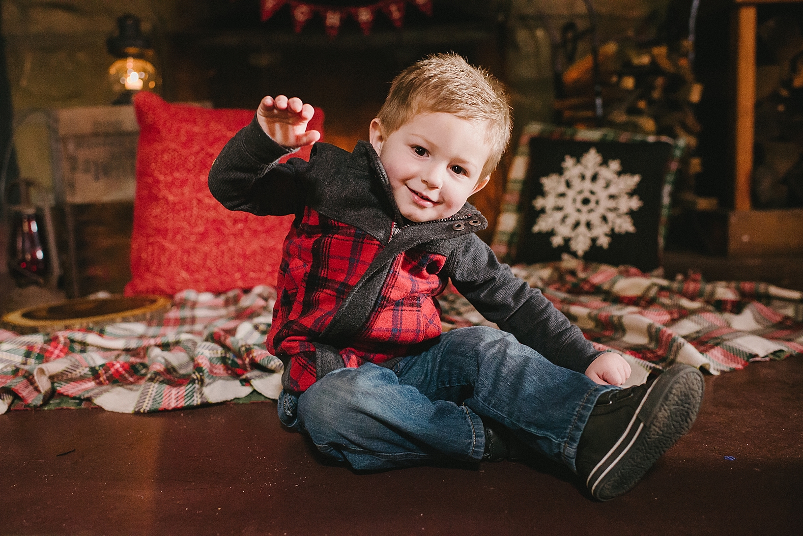 little boy in red and black flannel vest sitting on floor in front of fireplace