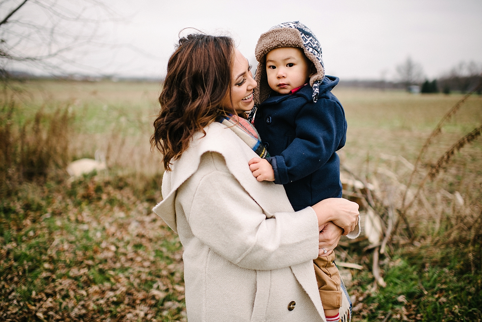mom wearing white winter coat holding toddler son in her arms wearing navy pea coat and warm fuzzy hat