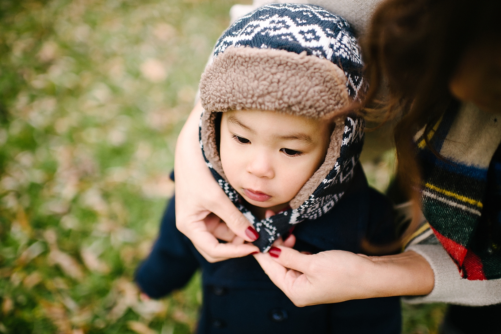 mother's hands tying toddler son's winter hat on