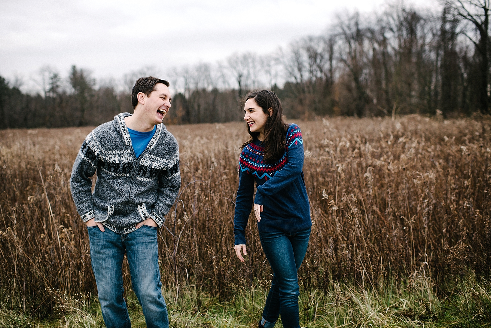 guy in grey sweater and girl in blue sweater laughing and playing in winter field