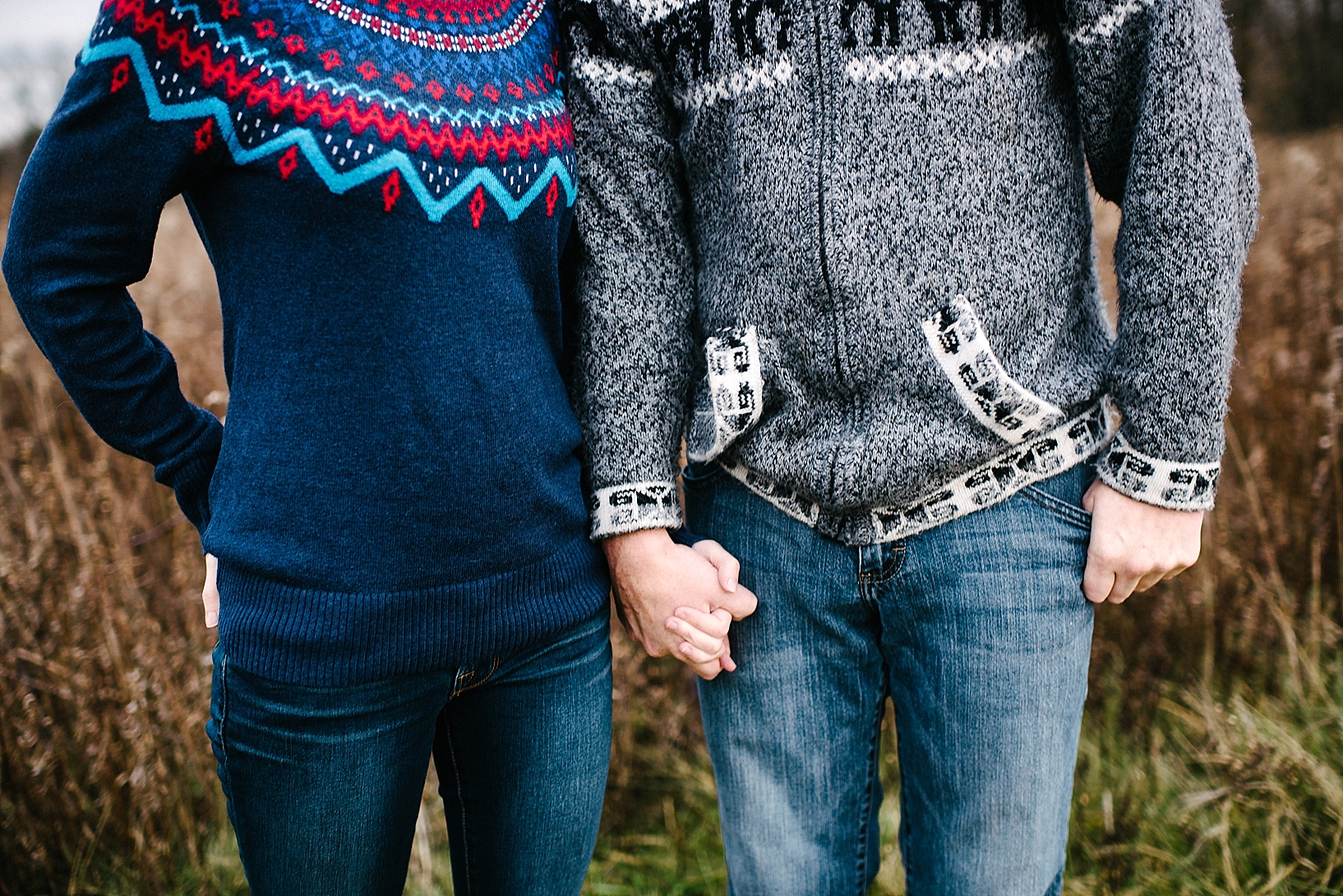 couple standing side by side holding hands wearing patterned winter sweaters