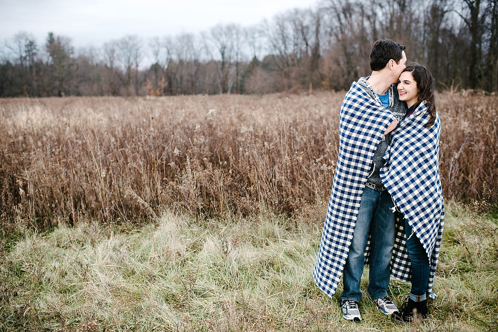 couple standing in field with blue checked blanket wrapped around them