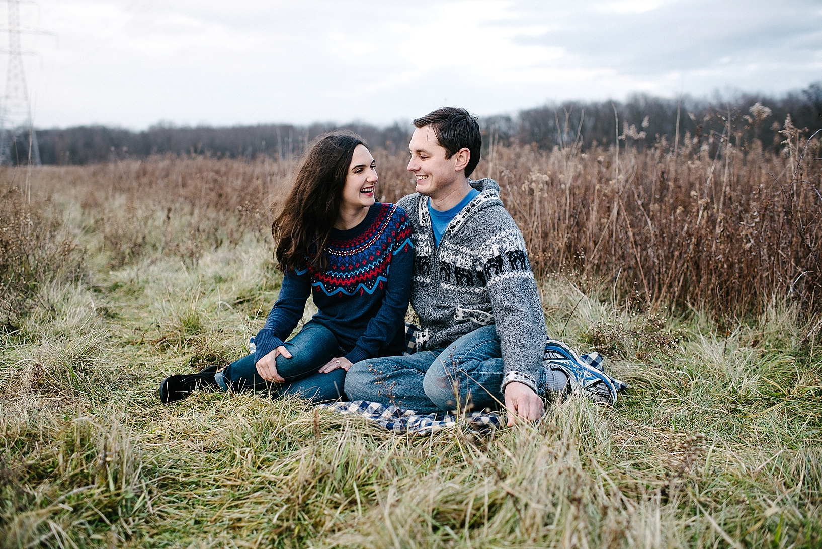 guy in grey sweater and girl in blue sweater sitting on blanket in field