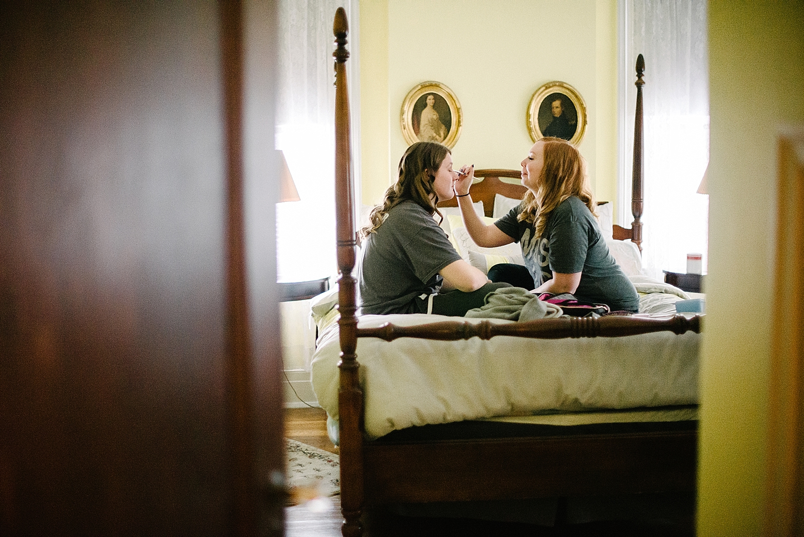 two girls sitting on four poster bed doing each other's makeup at old fashioned bed & Breakfast