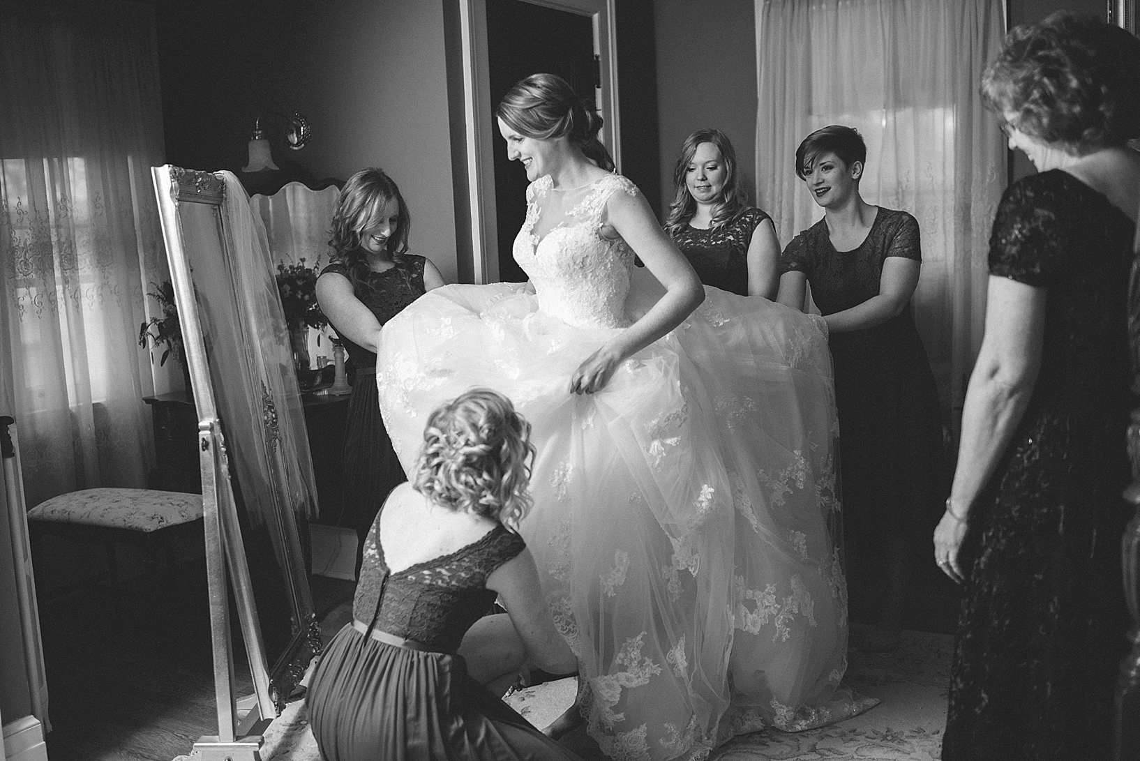 bridesmaids fluffing wedding gown as bride laughs