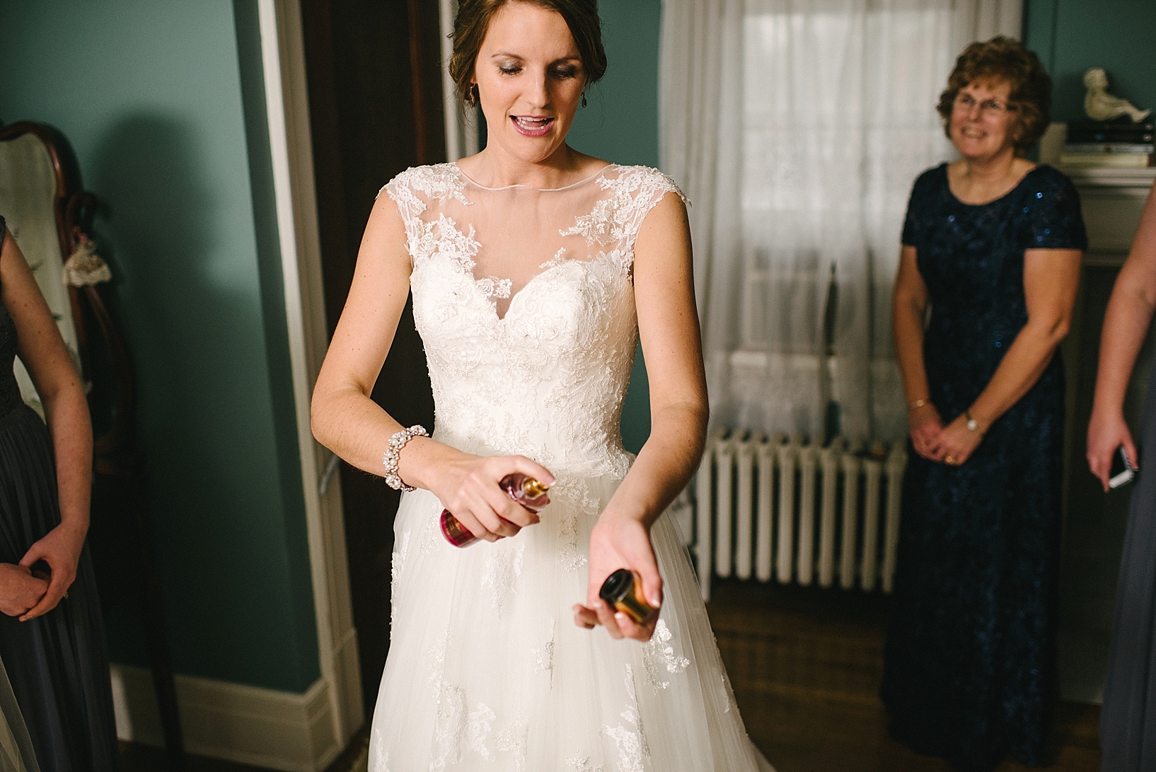 bride sprays perfume on her wrists as mother stands in background