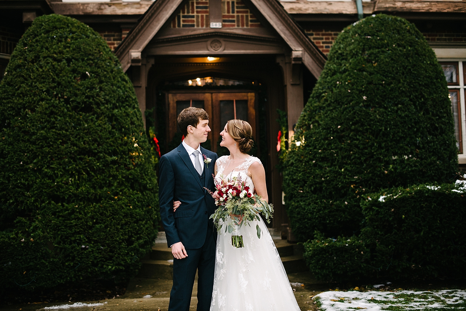 groom in navy suit and bride in lace wedding gown standing in front of chalet style bed & breakfast
