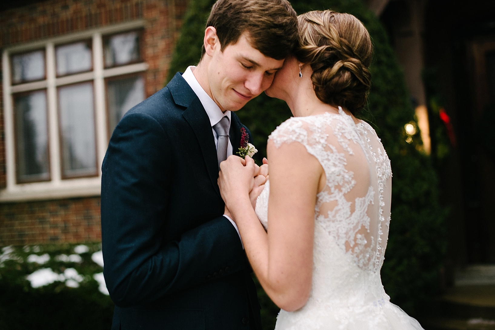 bride with updo and lace back wedding gown holding groom's hands and whispering in his ear