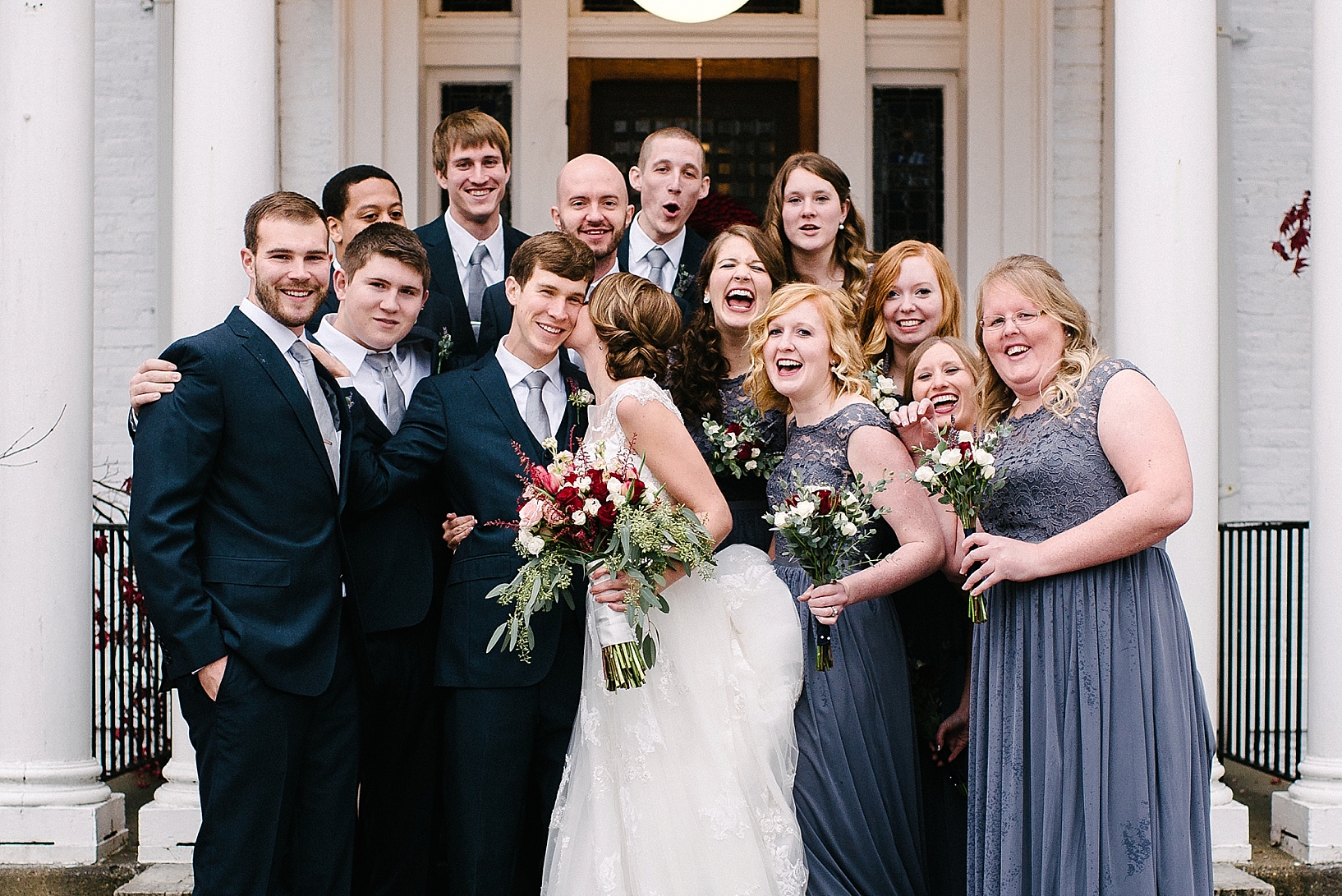 bridal party in navy and gray standing on steps of white house with pillars