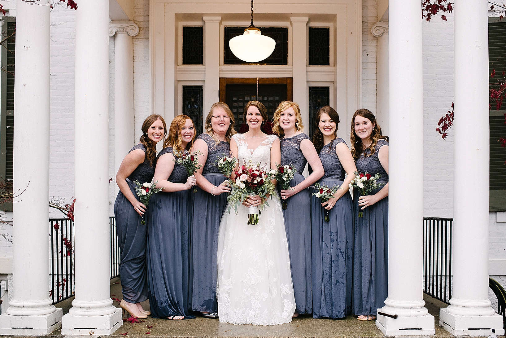 bride and bridesmaids in gray lace dresses standing on front porch of white home with tall pillars