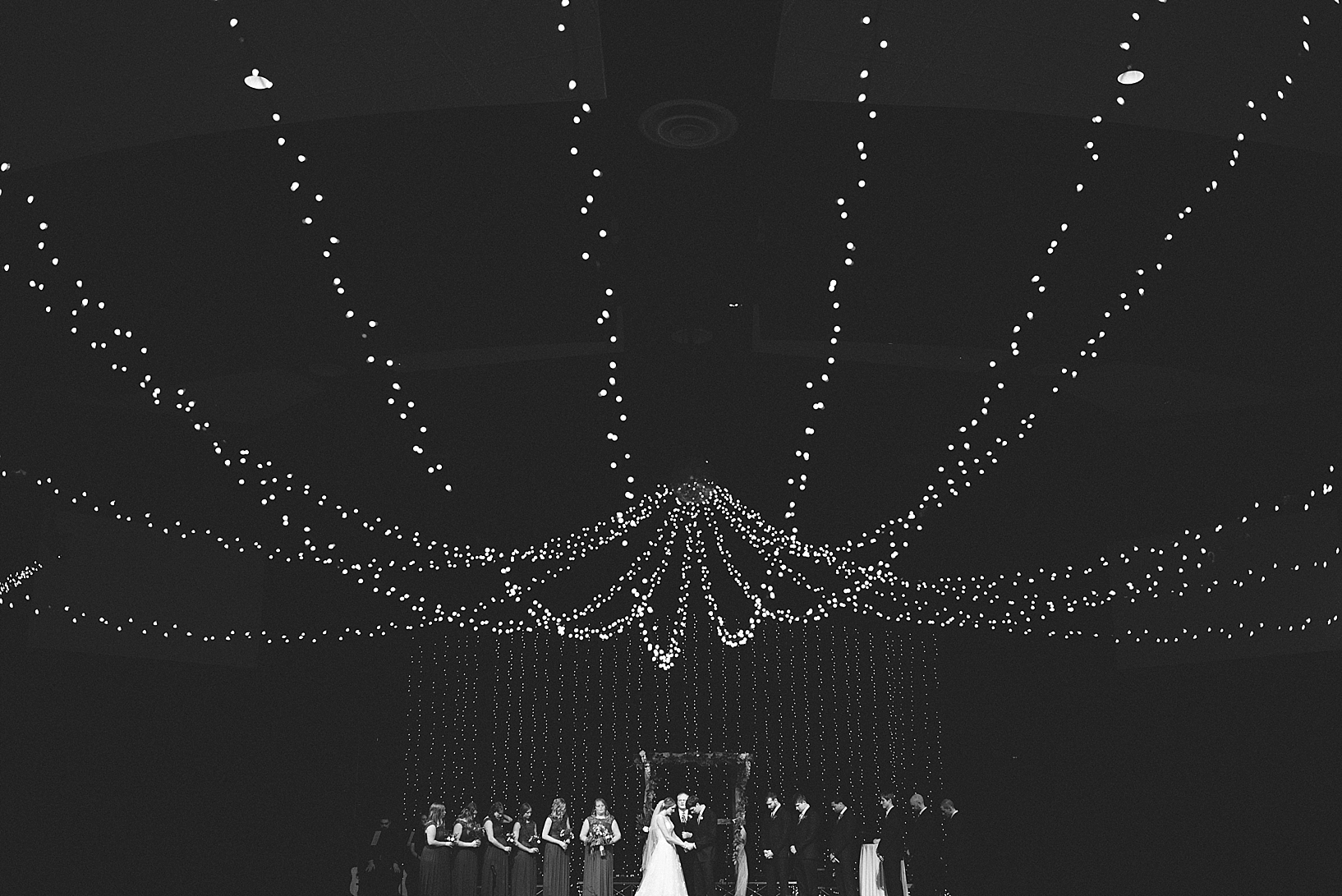 wedding party on church stage with twinkle lights hanging from ceiling