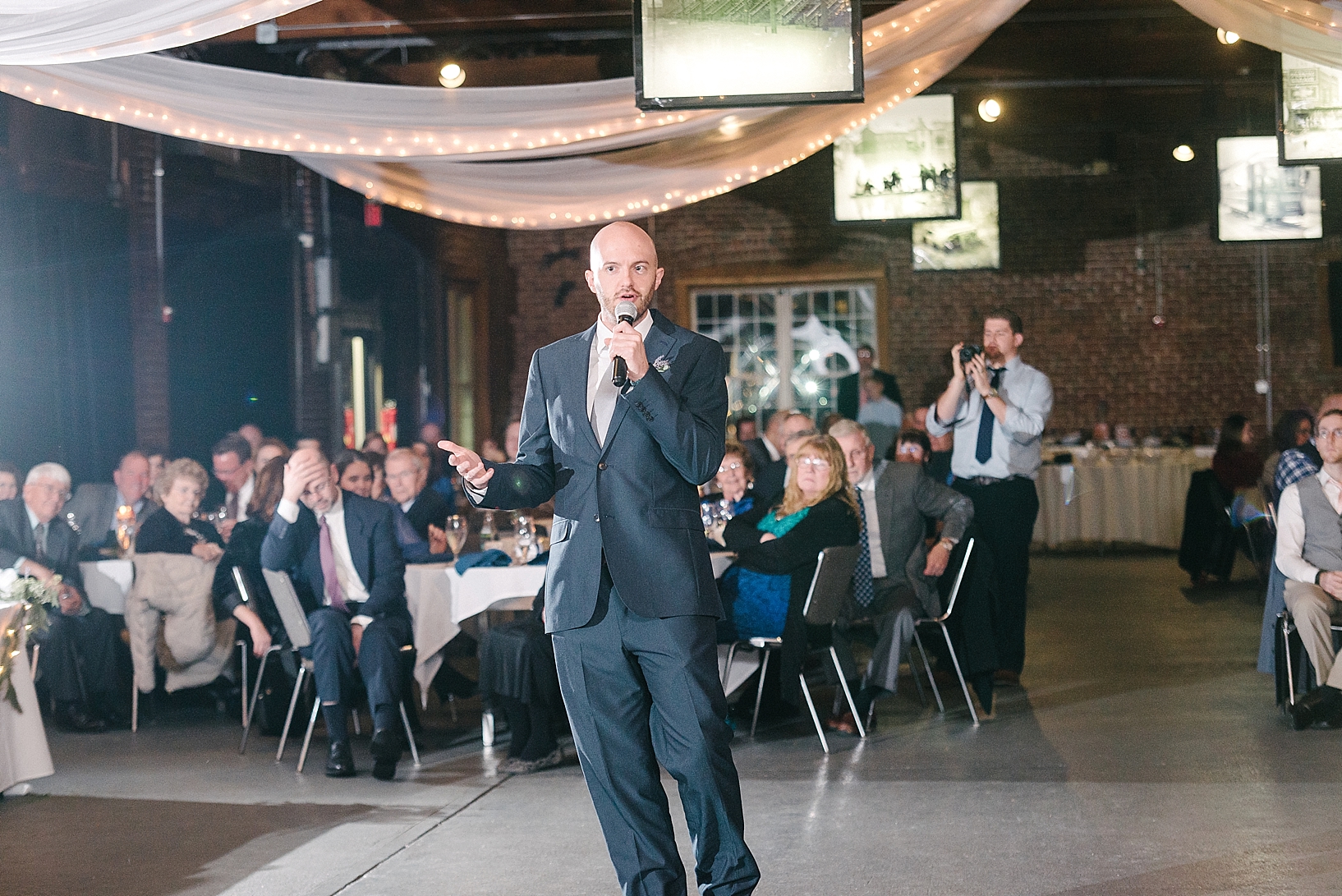 groomsman in navy suit giving toast during wedding reception