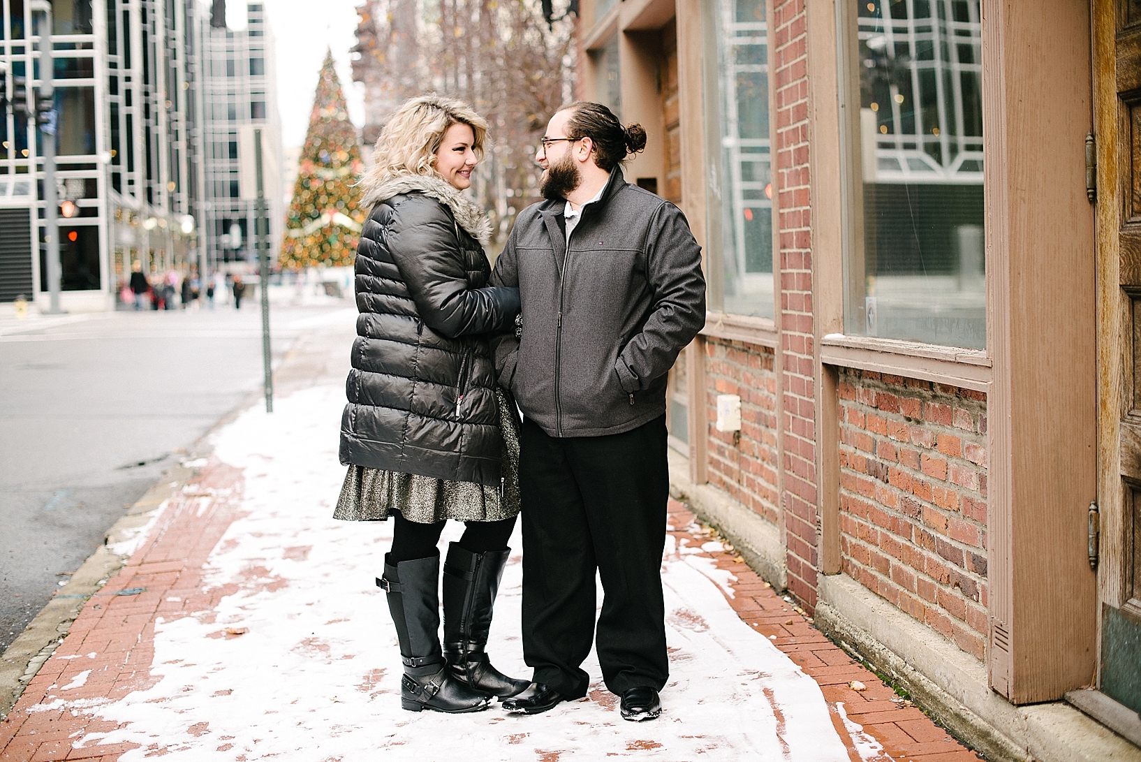 couple wearing winter coats standing on city sidewalk covered in snow