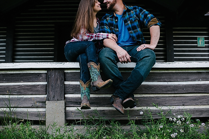 country couple in denim and flannel sitting on log cabin porch