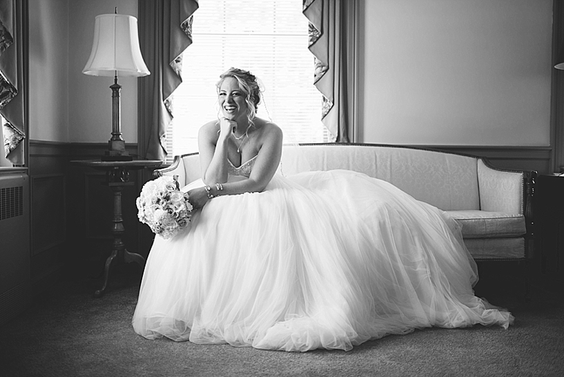 bride sitting on chaise laughing holding bouquet