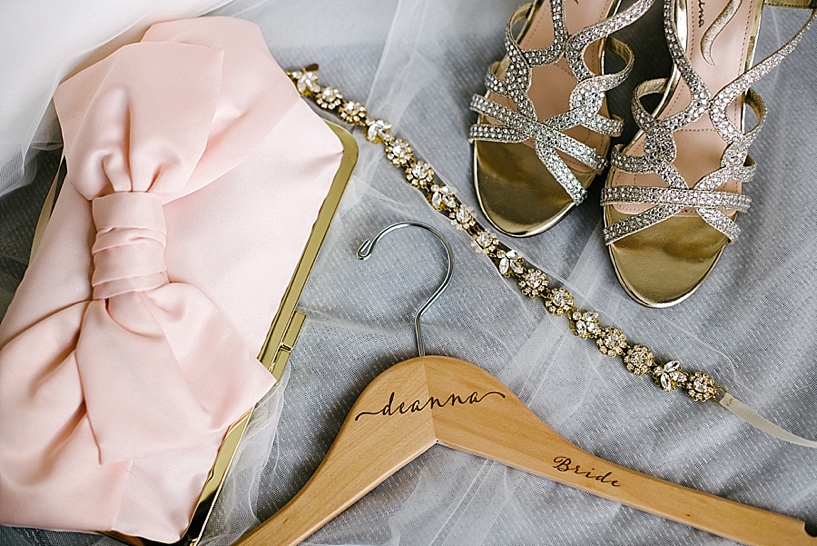 pink clutch, high heels, and wooden hanger sitting on lace veil
