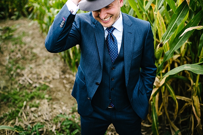 groom in navy suit and fedora standing in corn field