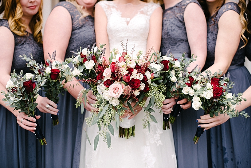 bridesmaids in grey lace dresses holding red and white bouquets