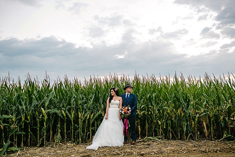 bride and groom stand side by side in front of corn field